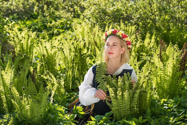Jonge vrouw in nationale kleding en krans op een groene varen Ligo Letse vakantie