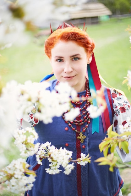 Jonge vrouw in Oekraïens nationaal kostuum Glimlachende jonge dame in traditionele kleding Blijf in de buurt van bloeiende boom Vrede in Oekraïne
