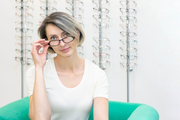 Jonge vrouw in optische winkel kiezen nieuwe bril met opticien. bril in de winkel van optica. Een vrouw kiest een bril. Emoties. Oogheelkunde.