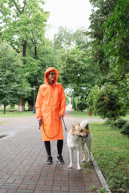 Jonge vrouw in oranje regenjas wandelen met haar hond in een park