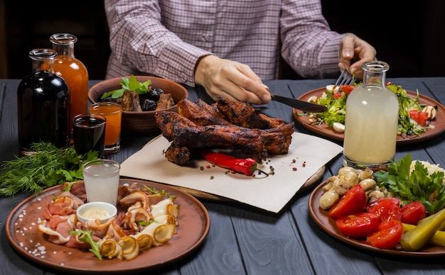 Jonge vrouw in overhemd en zwarte handschoenen begint gebakken ribben met peper en een fles wijn te eten