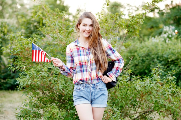 Jonge vrouw in plaid shirt en korte broek met Amerikaanse vlag