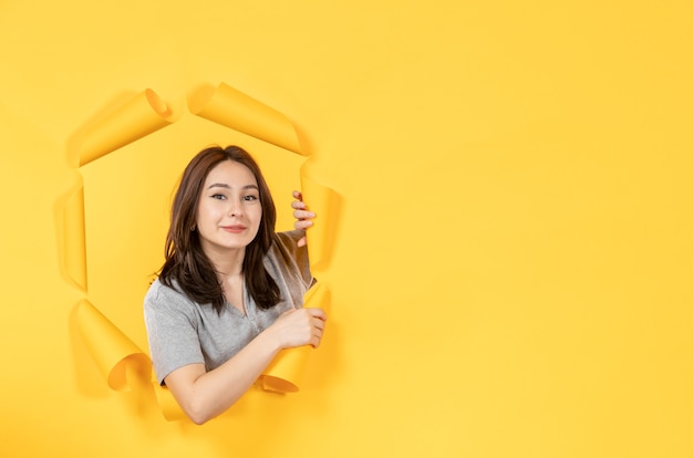 jonge vrouw in pyjama die door een gat in geel papier als achtergrond reclamevenster kijkt
