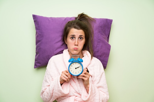 Jonge vrouw in pyjama die uitstekende klok houdt