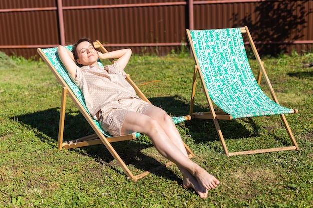 Jonge vrouw in pyjama rust in een stoel op een groen gazon op een zonnige zomerdag in het dorp en op het platteland