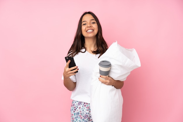 Jonge vrouw in pyjama's op de roze weg te halen koffie van de muurholding en mobiel