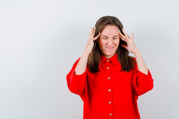 Jonge vrouw in rode blouse met vingers op tempels en ontevreden, vooraanzicht.