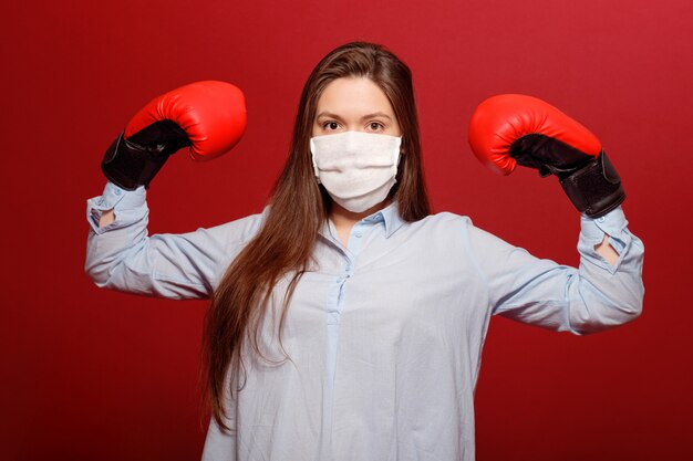 Jonge vrouw in rode bokshandschoenen op rode muur in beschermend medisch masker