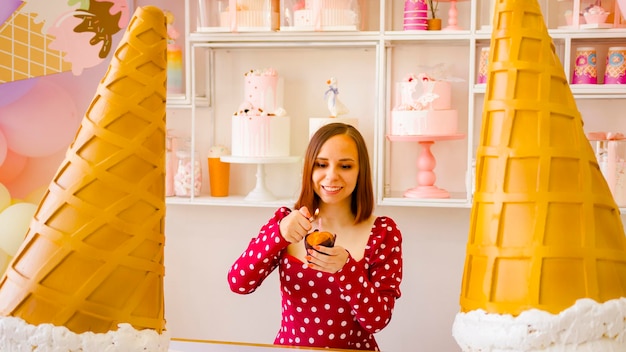 Jonge vrouw in rode jurk die kaars aansteekt in muffin Portret van gelukkige dame die verjaardag viert in zoetwaren