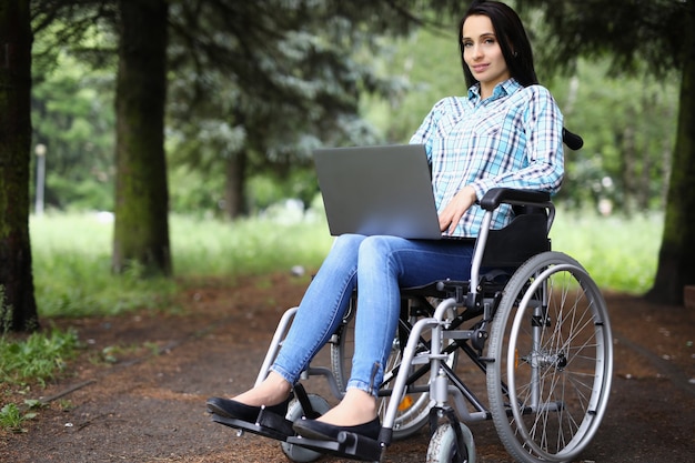 Jonge vrouw in rolstoel die aan laptop in park werkt