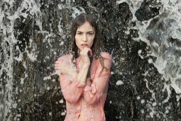 jonge vrouw in roze shirt staat onder water jets in waterval