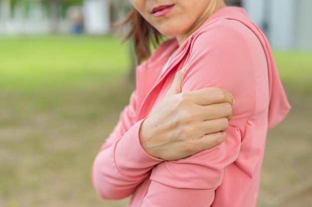 Foto jonge vrouw in roze sportoutfits verwondde haar bovenarm tijdens het sporten in het park bovenste gedeelte van sportmeisje dat aan armpijn lijdt terwijl ze aan het trainen is ongeval van oefeningsconcept