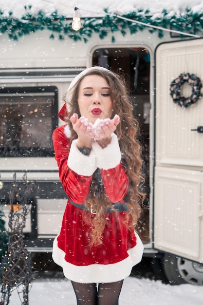 Jonge vrouw in santakostuum versiert de kerstboom op de wintercamping en maakt zich klaar voor de n