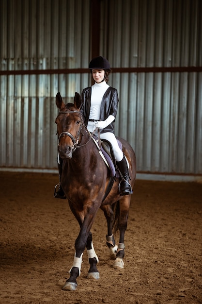 Jonge vrouw in speciaal uniform en helm paardrijden paardensport