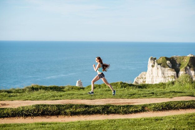 Jonge vrouw in sportkleding die buiten loopt op de prachtige rotsachtige kustlijn met prachtig uitzicht op de oceaan in de buurt van de stad Etretat in Frankrijk