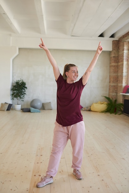 Jonge vrouw in sportkleding die haar handen opheft en glimlachend uitoefent zij in dansstudio