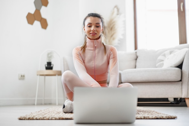 Jonge vrouw in sportkleding die laptop gebruikt om trainingsvideo-tutorials thuis te bekijken