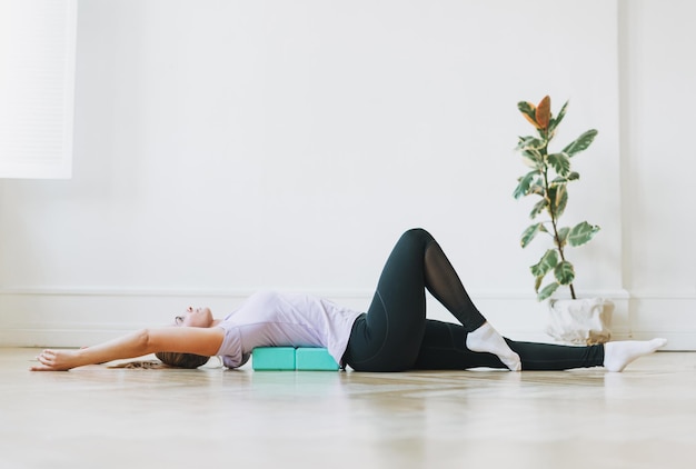 Jonge vrouw in sportuniform die zich uitstrekt op fitnessblokken die op de vloer liggen in een lichte studio