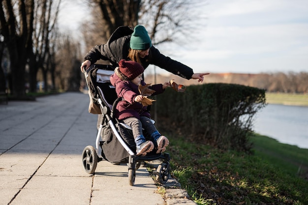 Jonge vrouw in stadspark met kinderwagen Warm herfstweer voor buitenactiviteiten