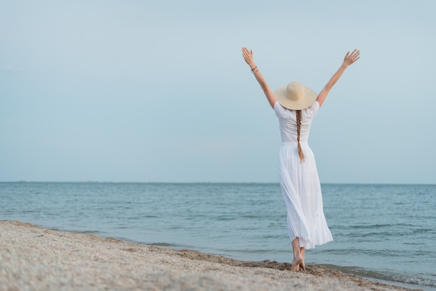 Jonge vrouw in strooien hoed en witte jurk wandelingen langs het strand.