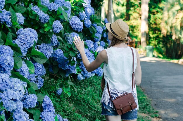 Jonge vrouw in strooien hoed in de buurt van weelderige blauwe wandeling in de zomer Park achteraanzicht