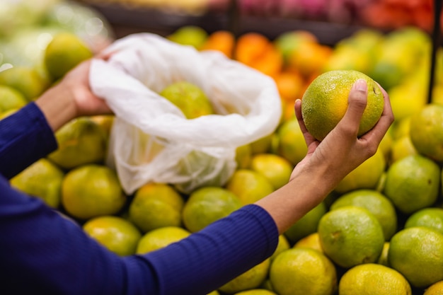 Jonge vrouw in supermarkt die sinaasappel koopt