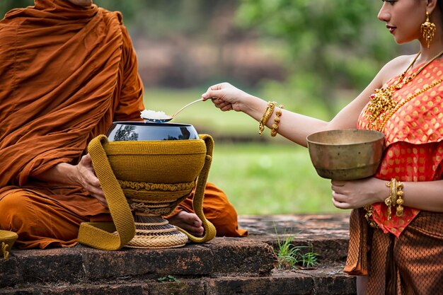 Foto jonge vrouw in traditionele kleding die gekookte rijst uit een container neemt door een monnik