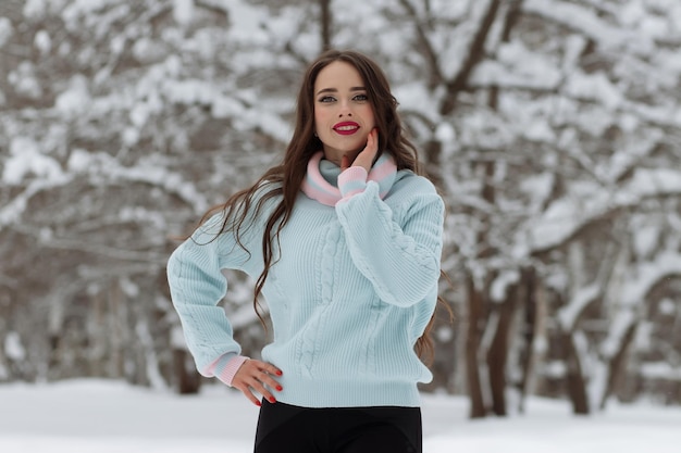 Jonge vrouw in trendy warme kleren die lacht voor de camera en lang haar aanpast