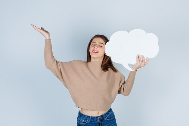 Jonge vrouw in trui, jeans die palm spreidt, papieren tekstballon vasthoudt en er gelukkig uitziet, vooraanzicht.