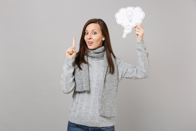 Jonge vrouw in trui, sjaal met wijsvinger omhoog met geweldig nieuw idee, zeg wolk met gloeilamp geïsoleerd op een grijze achtergrond. Gezonde mode levensstijl mensen oprechte emoties, koude seizoen concept.