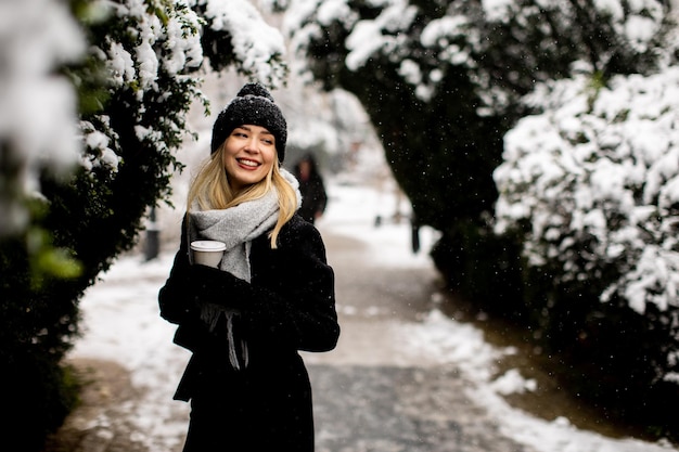 Jonge vrouw in warme kleren genietend in de sneeuw met afhaalkoffiekopje