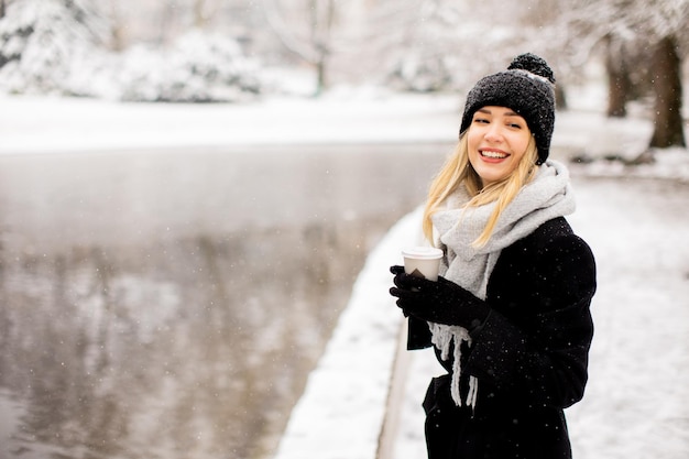 Jonge vrouw in warme kleren genietend in de sneeuw met afhaalkoffiekopje