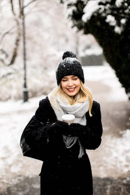 Jonge vrouw in warme kleren genietend in de sneeuw met afhaalkoffiekopje