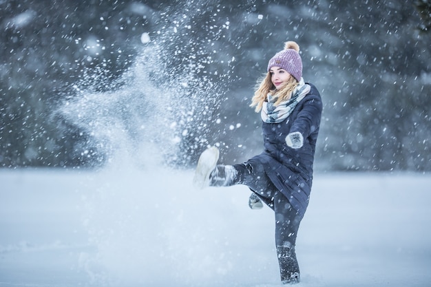 Jonge vrouw in warme kleren heeft plezier uit de sneeuw.