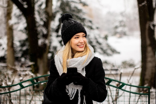 Jonge vrouw in warme kleren met behulp van mobiele telefoon op een winterdag