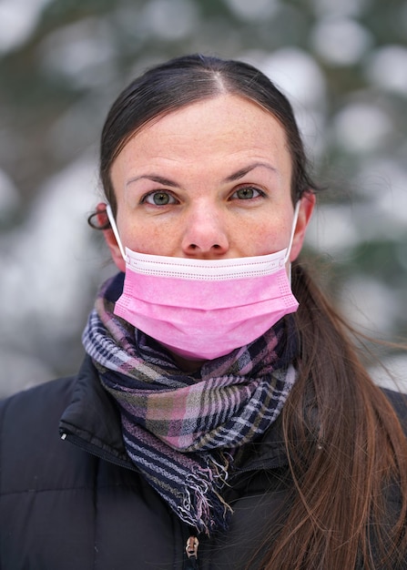 Jonge vrouw in warme winterkleding met een roze wegwerp-virusmasker onjuist, haar neus niet bedekt