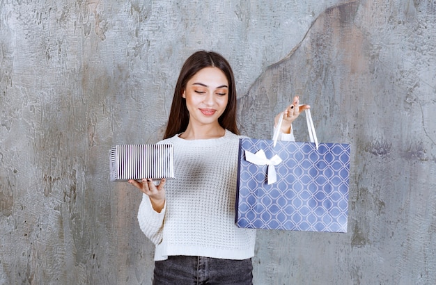 Jonge vrouw in wit overhemd met een zilveren geschenkdoos en een blauwe boodschappentas