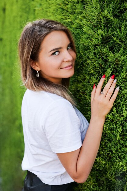 Jonge vrouw in wit overhemd met natuurlijke make-up bij groene haag