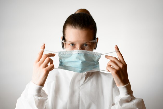 Foto jonge vrouw in witte beschermende pak en bril zet op medisch masker