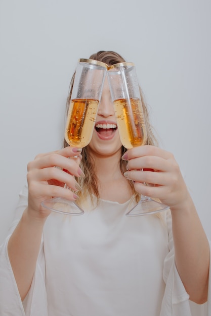 Jonge vrouw in witte jurk en met twee glazen mousserende wijn in handen voor haar gezicht