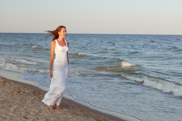 Jonge vrouw in witte kleren loopt langs de kust