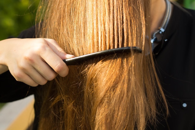 Jonge vrouw in zwarte blouse en zilveren ketting die haar rechte bruine haar van groene bomen kamt