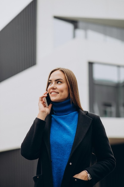 Jonge vrouw in zwarte jas die telefoon gebruikt
