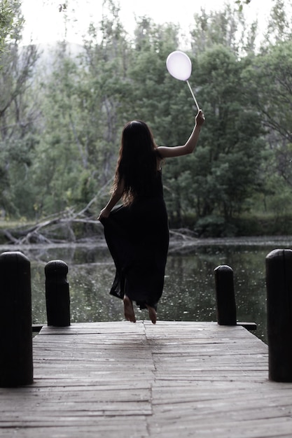 Jonge vrouw in zwarte jurk met een ballon in het bos