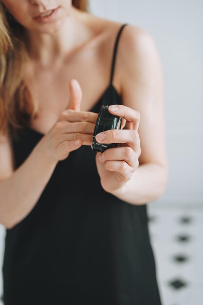 Foto jonge vrouw in zwarte jurk zet dagcrème lichaamscrème op een schone, frisse huid in de badkamer thuis