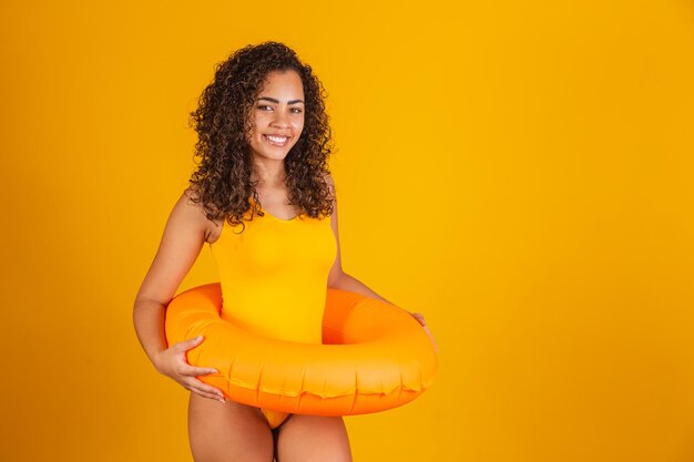 Jonge vrouw in zwembroek met oranje vlotter met een blij gezicht dat staat en lacht met een zelfverzekerde glimlach die tanden laat zien. Vakantie en leuk concept