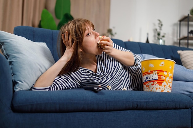 Jonge vrouw is gefocust op het kijken naar een film die popcorn eet