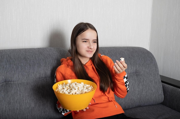 Jonge vrouw kijken naar een grappige show op tv met popcorn in haar handen glimlachend