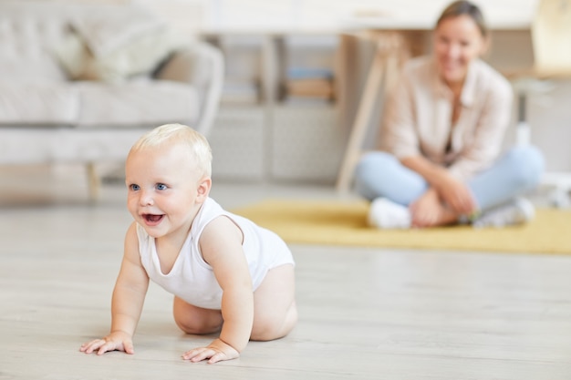 Jonge vrouw kijken naar haar vrolijke zoontje kruipen op zijn handen en voeten thuis