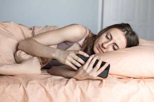 Jonge vrouw kijken naar het slimme telefoonscherm met vermoeide ogen in bed